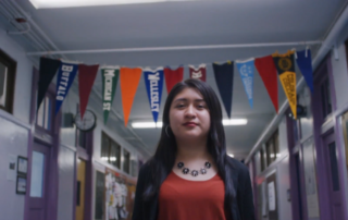 Cinthia Ibarra walks through a school hallway with college banners hanging behind her.